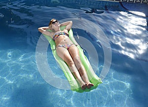 Young happy beautiful woman in bikini and sunglasses lying relax on float airbed at vacation hotel resort swimming pool