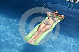 Young happy beautiful woman in bikini and sunglasses lying relax on float airbed at vacation hotel resort swimming pool