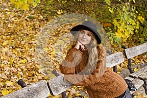 Young happy beautiful woman with curly hair wearing black hat and sweather having good time in autumn park