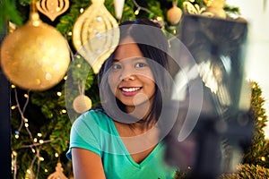 Young happy beautiful woman doing selfie on mobile phone on background illuminated christmas tree