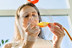 Young happy beautiful woman eating orange slice at home near the window