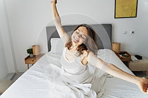 Young happy beautiful woman stretching while sitting on bed in the morning