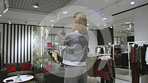 Young happy beautiful woman is taking a photo of herself dressed in grey suit at clothing store, tracking shot, 360
