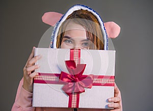 Young happy and beautiful woman in winter warm hoodie holding Christmas or birthday present box with ribbon in her hands smiling c