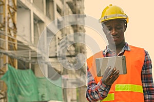 Young happy black African man construction worker smiling while using digital tablet at building site