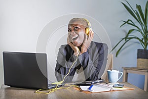 Young happy black afro american woman listening to music with headphones excited and joyful working at laptop computer desk at mod