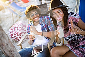 Young happy black couple with drinks relaxing on the beach