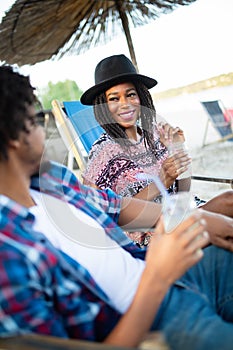 Young happy black couple with drinks relaxing on the beach