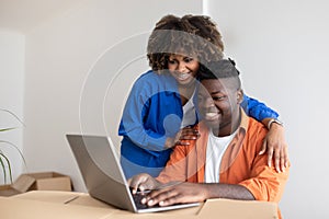 Young Happy Black Couple Using Laptop In Their New Home After Moving