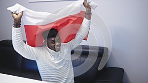 Young happy black man man with polish flag watching footbal game on tv