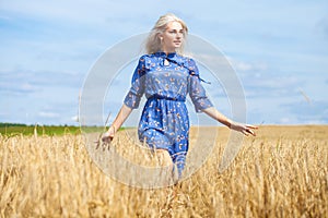 Young happy blonde in a blue dress posing in a wheat field