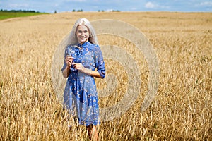 Young happy blonde in a blue dress posing in a wheat field