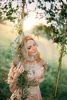 Young happy blonde woman in image of a forest nymph in a light peach vintage dress, stands near a tree. Fashion model