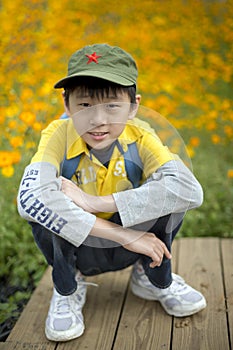 Young happy boy squatting at field of flowers