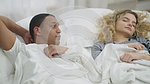 Young happy boyfriend admiring sleeping girlfriend and looking at camera smiling. Portrait of loving African American