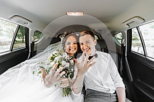young happy bride and groom are rejoicing after the wedding ceremony in their car