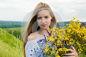 Young happy bride holding bouquet of blooming yellow flowers in countryside. Picture of beautiful happy girl with long light hair