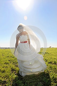Young happy bride in long white dress walking on green field