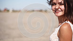 Young happy bride smiling, walking at desert landscape. Pretty woman with dark hair blowing in the wind at photoshoot