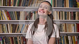 Young happy brunette girl is standing in library, laughing