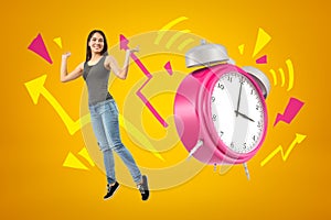 Young happy brunette girl wearing casual jeans and t-shirt with pink alarm clock and cartoon arrows on yellow background