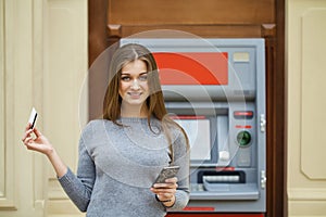 Young happy brunette woman withdrawing money from credit card at