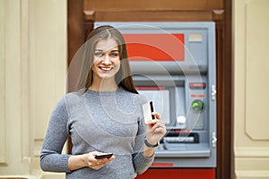 Young happy brunette woman withdrawing money from credit card at