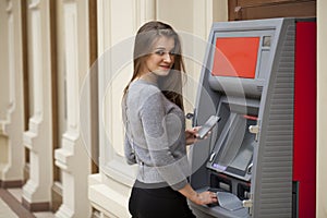 Young happy brunette woman withdrawing money from credit card at