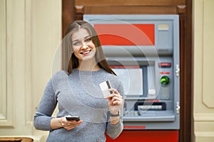 Young happy brunette woman withdrawing money from credit card at