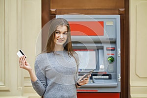 Young happy brunette woman withdrawing money from credit card at