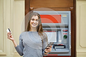 Young happy brunette woman withdrawing money from credit card at