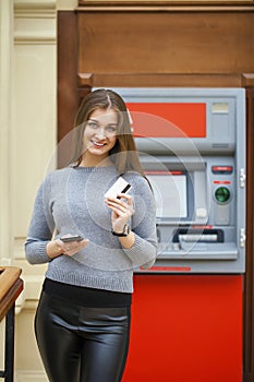 Young happy brunette woman withdrawing money from credit card at