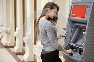Young happy brunette woman withdrawing money from credit card at photo