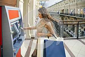 Young happy brunette woman withdrawing money from credit card at photo