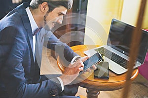 Young happy businesman working at cafe, using mobile phone