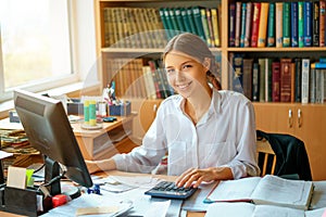 Young happy business lady in white shirt sitting at table with computer and papers working environment