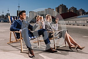 young happy business people relaxing on sunbeds and clinking glasses with coffee to go photo