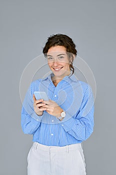 Young happy business woman holding mobile phone standing at gray wall.