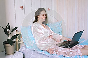 Young happy business woman lies in bed in pajamas in a cozy home. Online working, studying from home with laptop. Freelancer