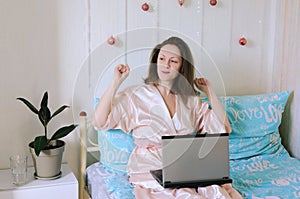 Young happy business woman lies in bed in pajamas in a cozy home. Online working, studying from home with laptop. Freelancer