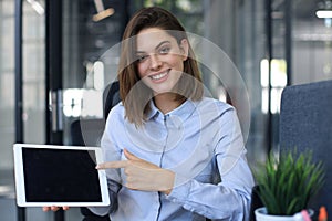 Young happy business woman showing blank tablet computer screen in office
