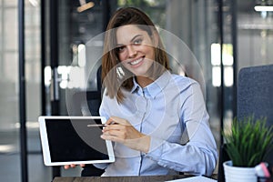 Young happy business woman showing blank tablet computer screen in office