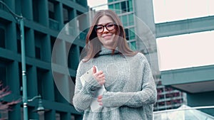 Young happy business woman or student standing in city holding digital tablet.