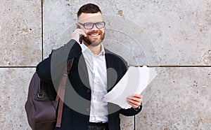 Young happy businessman in formal clothes speaking on mobile phone with client or partner outside