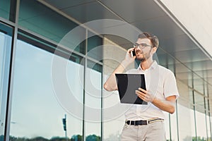 Young happy businessman making a call and holding clipboard