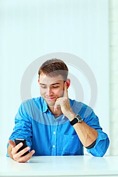 Young happy businessman sitting at the table and holding smartphone