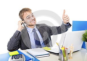 Young happy businessman smiling confident talking on mobile phone at office computer desk