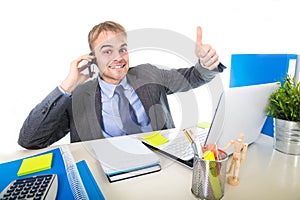 Young happy businessman smiling confident talking on mobile phone at office computer desk