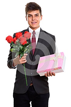 Young happy businessman smiling while holding red roses and gift