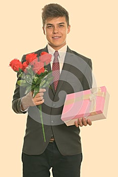 Young happy businessman smiling while holding red roses and gift box ready for Valentine's day